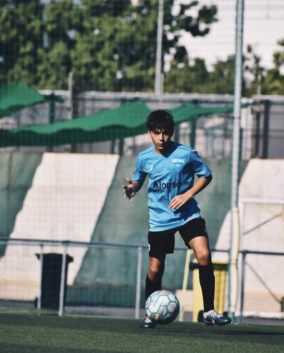 FFS player in a light blue kit with the Future Football Stars crest dribbling a ball